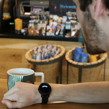 A person sitting in a coffee shop looking at a smartwatch, which displays the direction of a sound occurring in their vicinity. Copied here for decorative purposes.